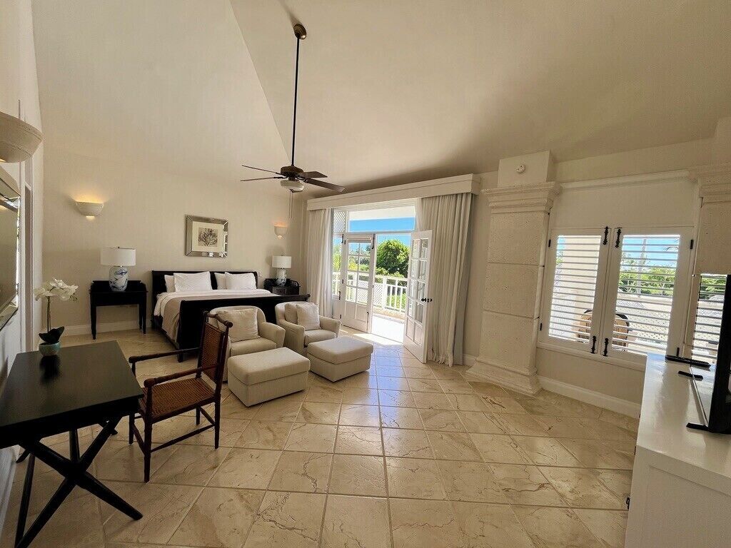 A spacious room with a bed, a desk, a chair, a sofa, and a balcony with curtains.