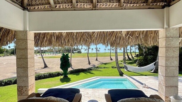 Un espacio exterior techado con piscina, mobiliario de mimbre y vistas a un jardín ajardinado.