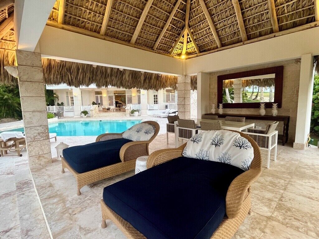 A poolside lounge area with wicker furniture and a thatched roof.