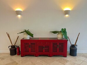 Un gabinete rojo con dos luces fijadas a la pared, dos plantas en macetas y dos contenedores metálicos con ramas.