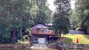 Eine Holzhütte am See mit einer Terrasse und einer Garage.