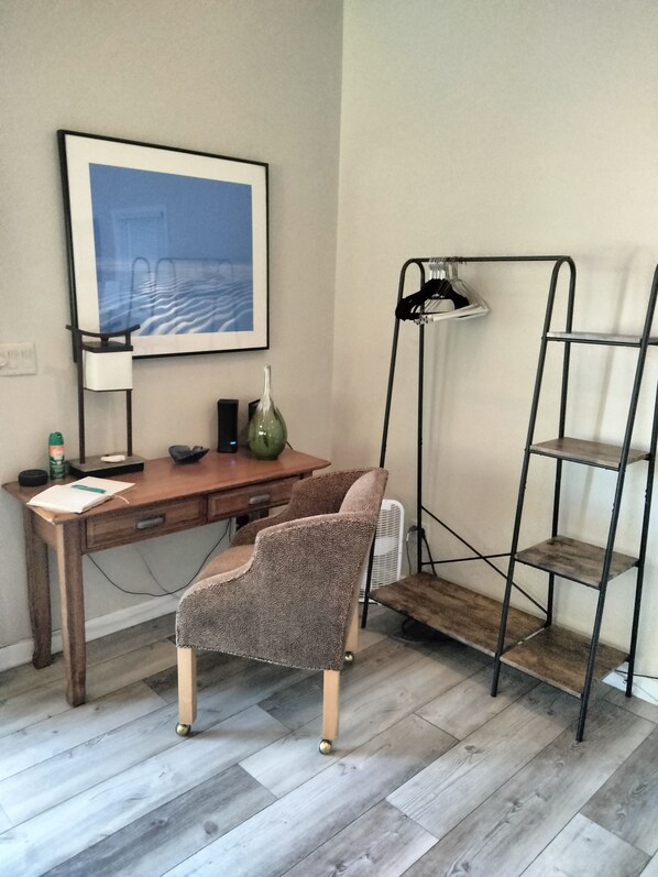 Una habitación con un escritorio de madera, una silla, una lámpara de pie, una estantería y un cuadro en la pared.