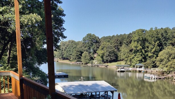 Eine Holzterrasse mit Kübelpflanzen, mit Blick auf einen stillen See mit Booten und einem Gazebo.