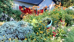 Ein Haus mit roter und weißer Fassade, umgeben von einem Garten mit verschiedenen Pflanzen und Blumen.