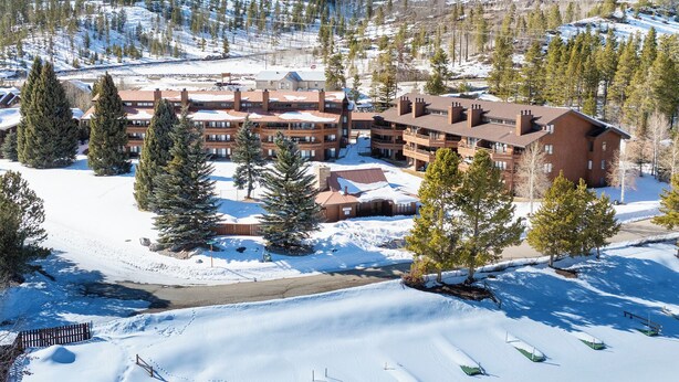 Un chalet à plusieurs étages, avec une piste de ski en arrière-plan.