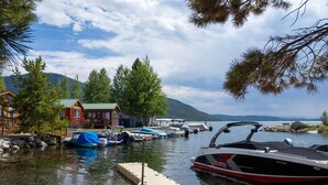Une jetée au bord du lac avec des bateaux, une plateforme en bois et un chalet doté d’un toit végétalisé.