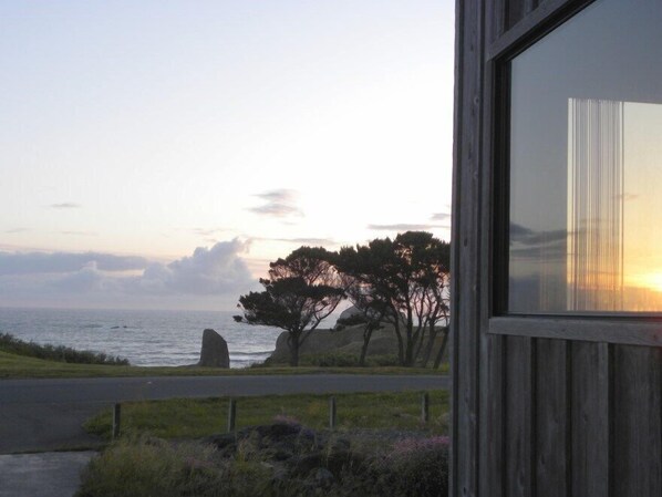 A coastal view with a road leading to a property with a wooden facade and a large window reflecting the sunset.