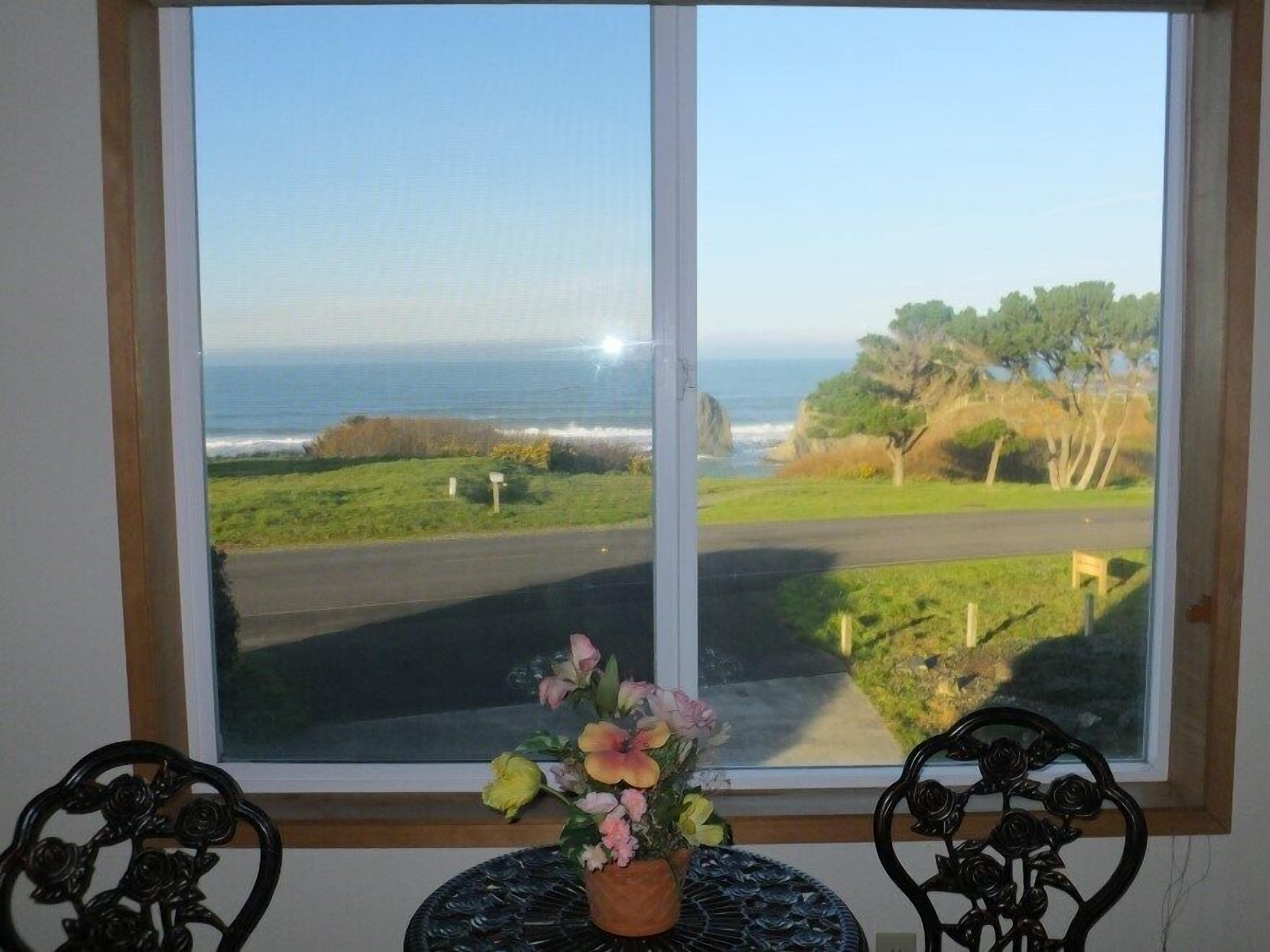 A room with a large window overlooking a coastal road and ocean.