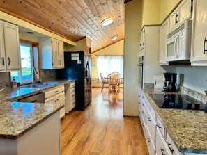A kitchen with granite countertops, white cabinets, a black refrigerator, and a dining area with a table and chairs. - All Sunsets & Surf 4 bedrooms (Bandon)