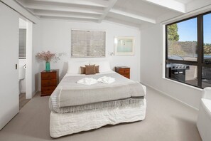 Quarto com uma cama grande, cômoda de madeira, mesa de cabeceira e janela com vista para o exterior.