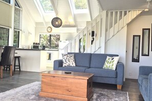 Uma sala de estar moderna com um sofá, uma mesa de centro e uma escada que leva a um andar superior.