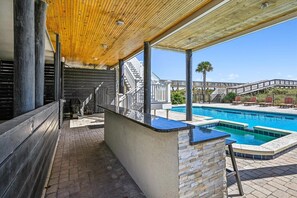 Relax by the pool on a shaded wooden ceiling-covered area with a comfortable bench and a sunbathing platform.