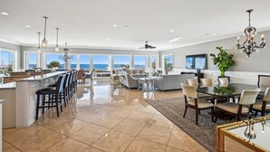 Una cocina amplia con una isla grande, un comedor con mesa de vidrio y una sala de estar con televisor grande y una planta.