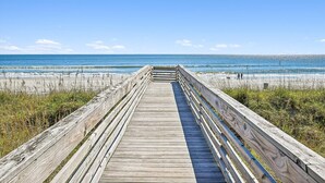Un paseo marítimo de madera que conduce a una playa, con cielos despejados.