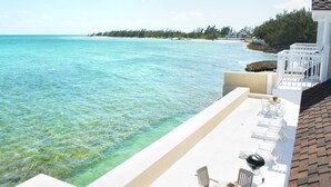 Terraço com mobiliário de exterior branco, vista para um mar azul límpido e uma praia.