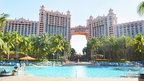 Um hotel grande com piscina central rodeada por palmeiras e espreguiçadeiras.