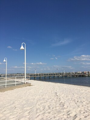 A beach with a pier extending into the water, featuring street lamps and a railing.