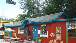 Un bâtiment rouge avec un toit bleu, un petit espace extérieur aménagé avec des sièges et une enseigne.