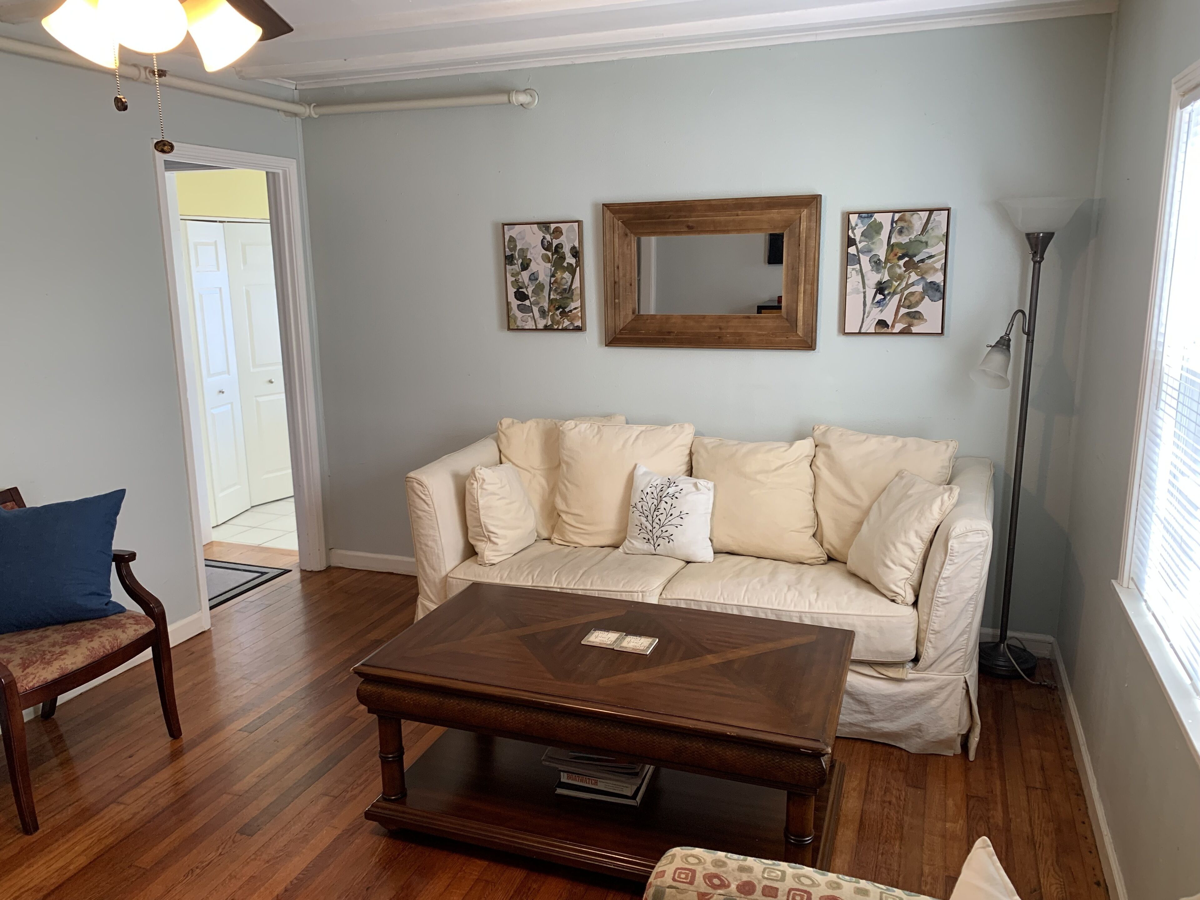 Un salon avec un canapé beige, une table basse en bois, un fauteuil bleu et un lampadaire.