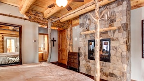 Ein Schlafzimmer mit einem großen Bett, Holzbalken, Steinwänden, einem Kruzifix an der Wand und einem Kamin.