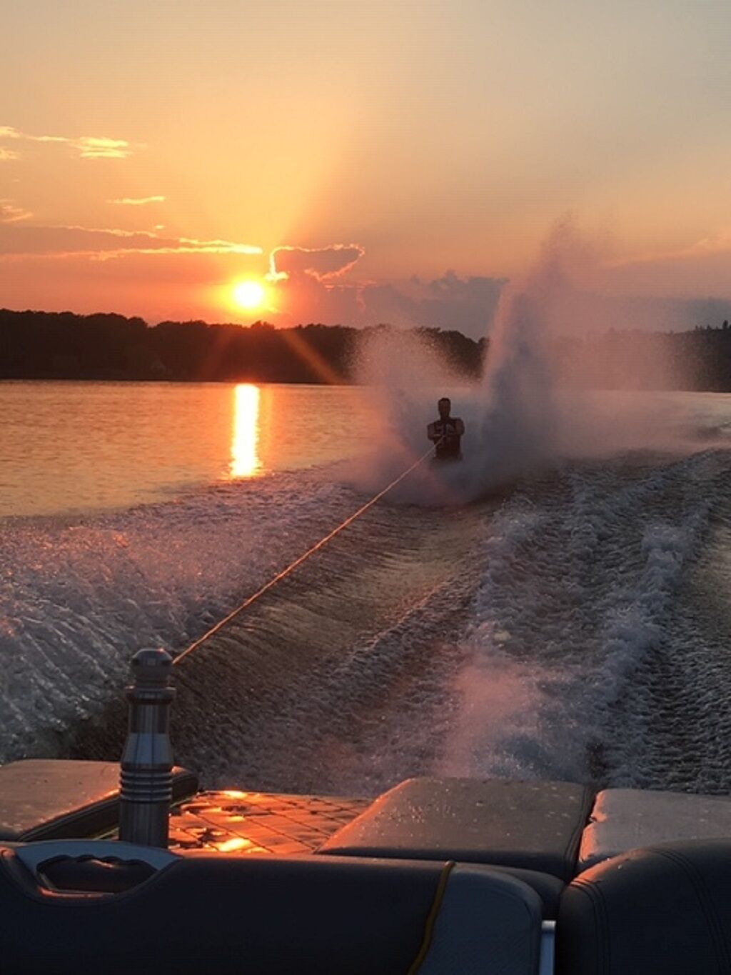 Une scène de ski nautique au coucher du soleil, où l’on aperçoit un bateau et un skieur.