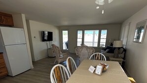 A dining area with a table, chairs, a ceiling fan, and a view of the beach through large windows.
