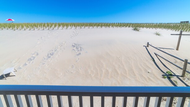 A sandy beach with footprints and a wooden fence.
