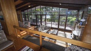 A spacious room with a large window overlooking a deck, wooden furniture, and a view of the outdoors.