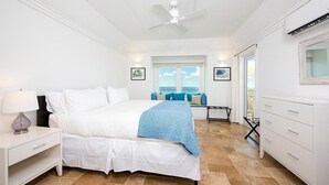 Ein Schlafzimmer mit Bett, Nachttisch, Kommode und Blick auf den Ozean.