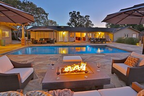 Ein Garten mit Swimmingpool, Sitzgelegenheit im Freien und einer Feuerstelle.