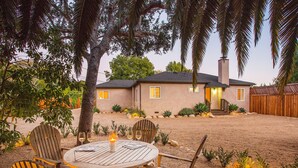 A patio with a round table and four wooden chairs, a house in the background, and a tree in the foreground. - Los Arboles Ranch - Recreational Dream Near Hope Ranch (Santa Barbara)