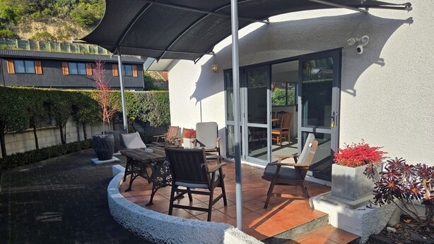 Eine Terrassenfläche mit Gartenmöbeln, ein überdachter Sitzbereich und Blick ins Innere durch Glastüren.
