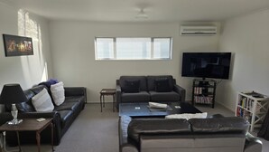 Ein Wohnzimmer mit Sofa, Couchtisch, Fernseher, Bücherregal und einer Lampe.