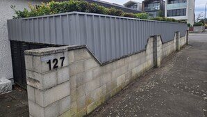 Ein Wohngebäude mit grauer Metallzaun, einer Betonmauer mit der Hausnummer 127 und moderner Architektur im Hintergrund.