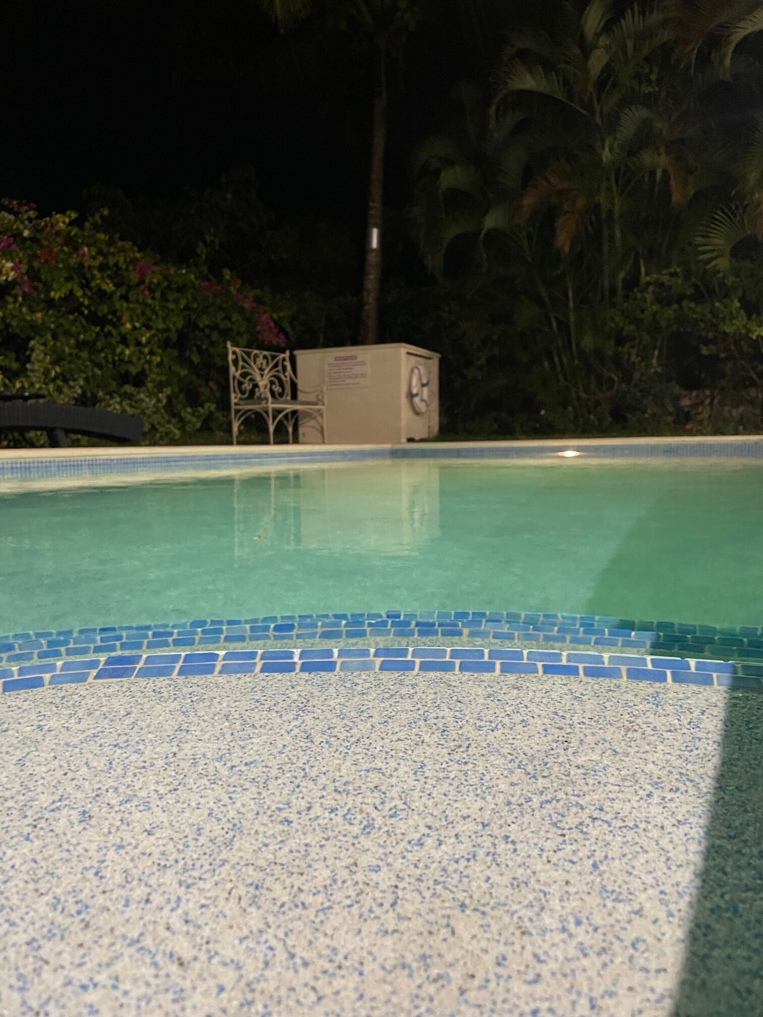 A swimming pool with a tiled edge and a chair in the background.