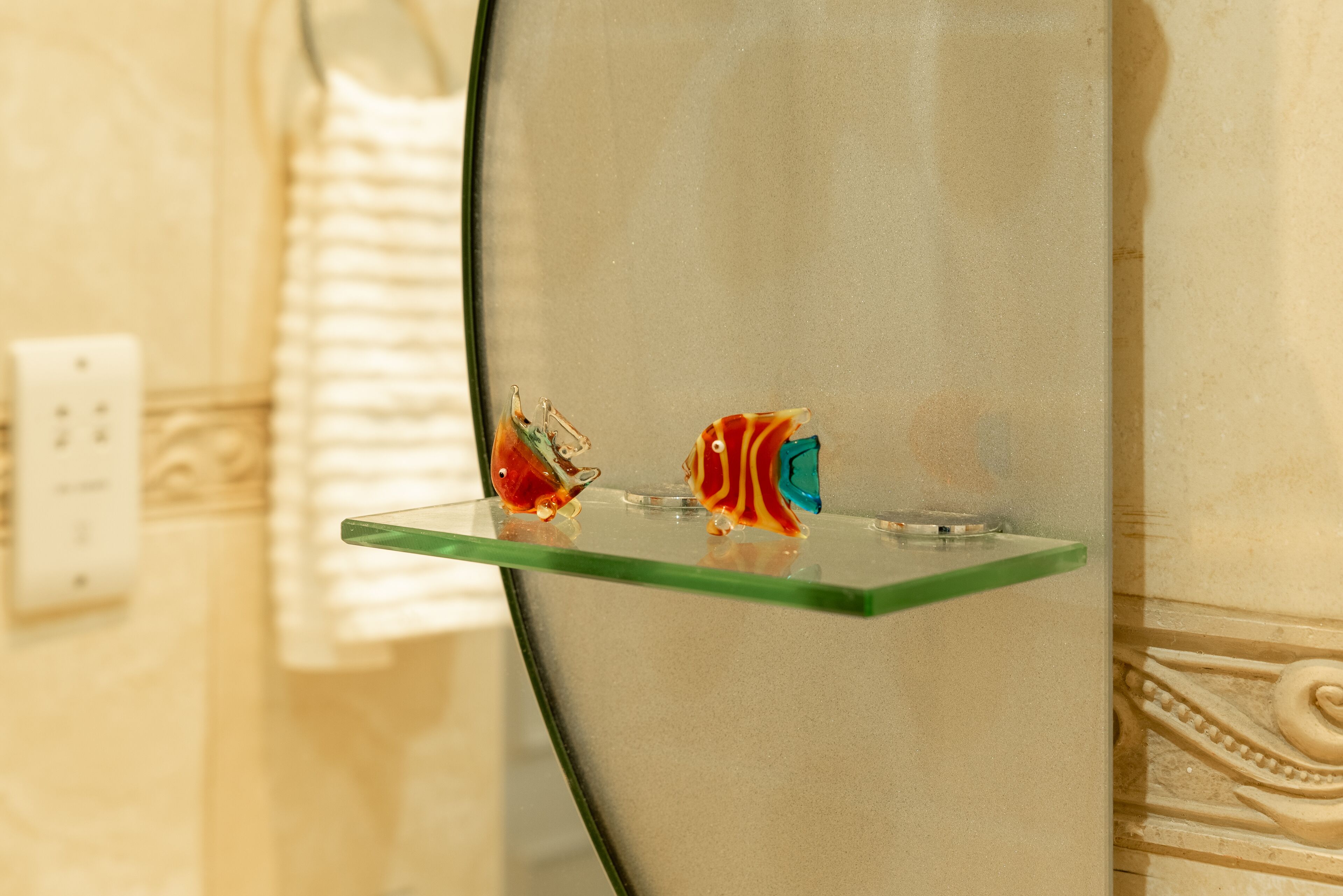 A bathroom with a glass shelf displaying two colorful glass fish figurines.