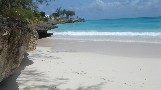 Ein Strand mit klarem türkisblauem Wasser, weißem Sand und Felsen.