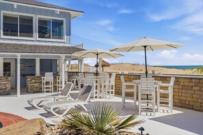 A two-story house with a patio area featuring white lounge chairs, umbrellas, and a pool.