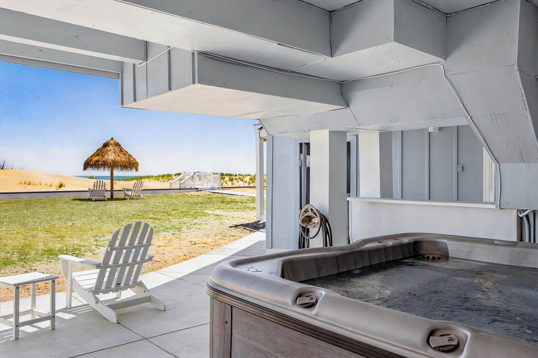 Zona d'hidromassatge exterior moderna amb vista a la platja, un para-sol de palla i cadires Adirondack.
