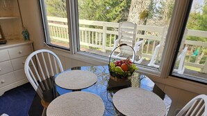 Une table à manger avec deux sets de table ronds en fibres tressées, des chaises blanches et un panier de fruits.