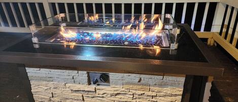 A rectangular outdoor fire feature with a glass top and stone base, surrounded by a white railing.