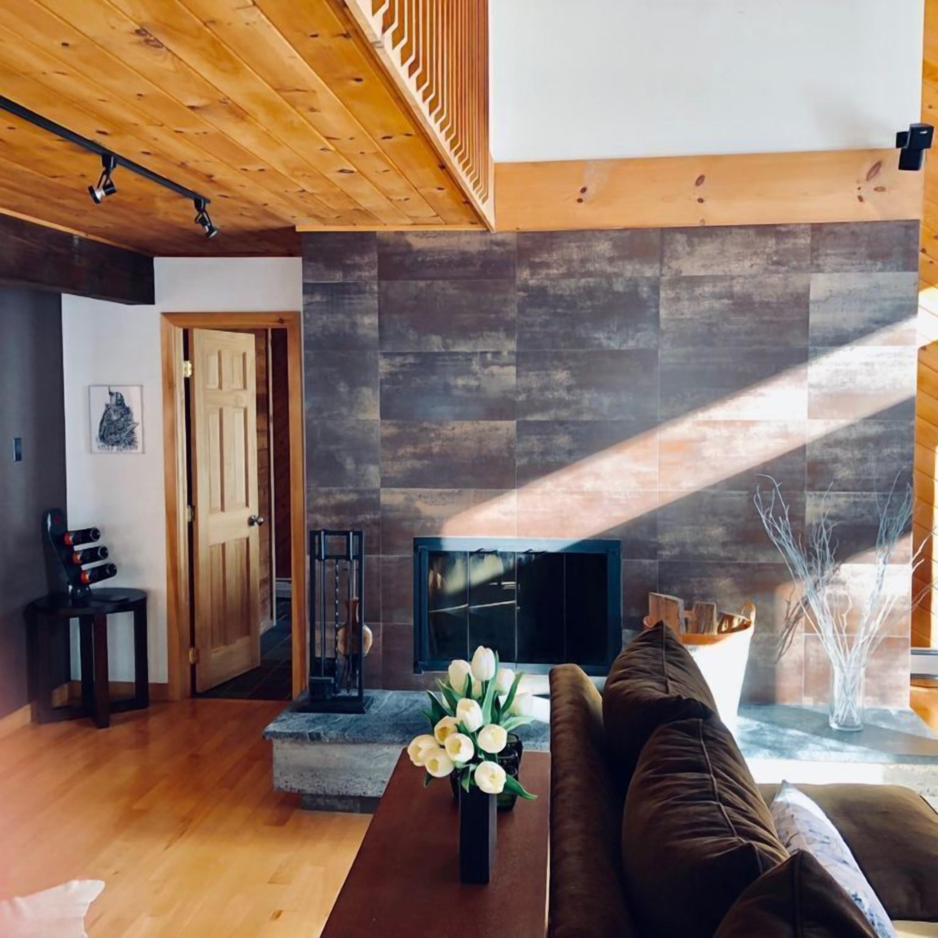 Een moderne woonkamer met een stenen open haard, houten vloeren en een bruine bank.