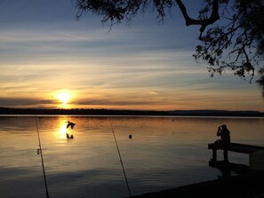 Ein ruhiger See bei Sonnenuntergang mit Angelruten und einer Bank.