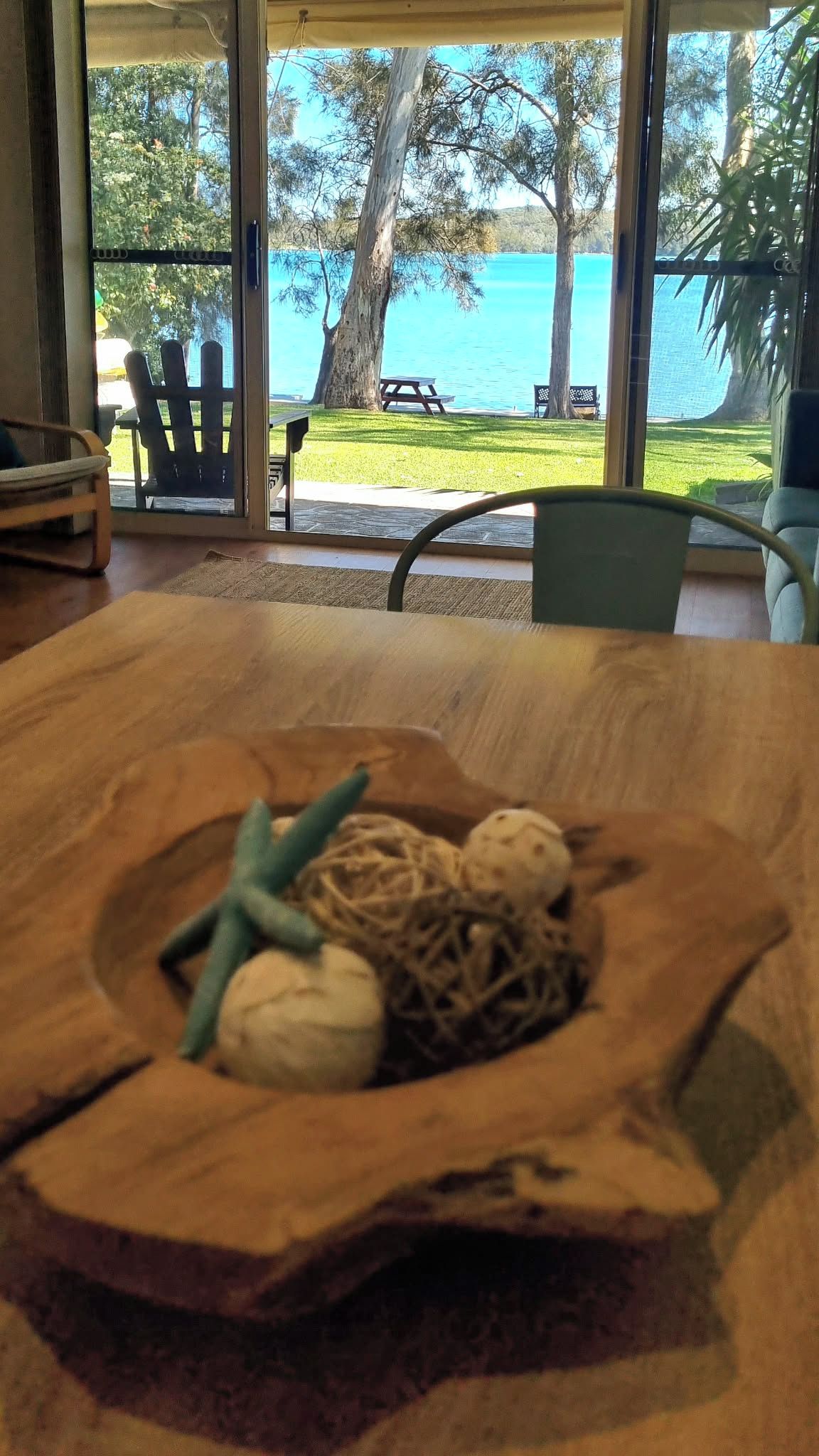 A wooden table with a nest-like centerpiece containing a green twig, a white spherical object, and a brown spherical object.