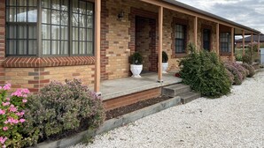 Una casa de un piso con fachada de ladrillo, un porche cubierto y un camino de entrada de grava.