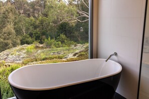 A modern bathroom with a freestanding bathtub, a large window offering a view of a natural landscape with trees and rocks. - Wollemi Retreat  (Rylstone)