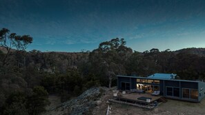 A modern house with a large deck, large windows, and a view of a forested area. - Wollemi Retreat  (Rylstone)
