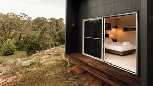 Un dormitorio moderno con un amplio ventanal corredera, una cama y una mesita de noche con lámpara.
