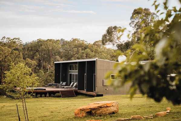 A modern house with a deck, surrounded by a grassy yard and trees. - Wollemi Retreat  (Rylstone)