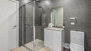 A modern bathroom with a glass-enclosed shower, a vanity with a sink and mirror, and a toilet. - Beachfront #12 Beach Access, Pool, PetFriendly (Sapphire Beach)